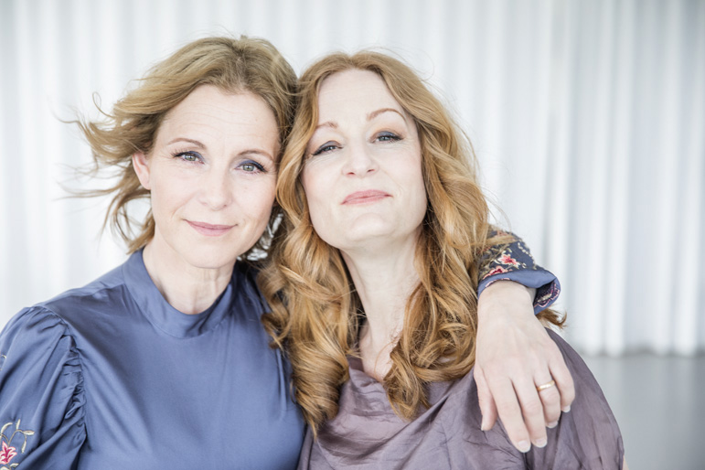 Helen Sjöholm and Anna Stadling in half figure with their arms around each other. 