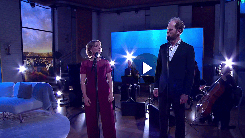 Helen Sjöholm och Fredrik Lycke sjunger i TV¤ Nyhetsmorgon. Foto i helfigur med blått bakgrundsljus.