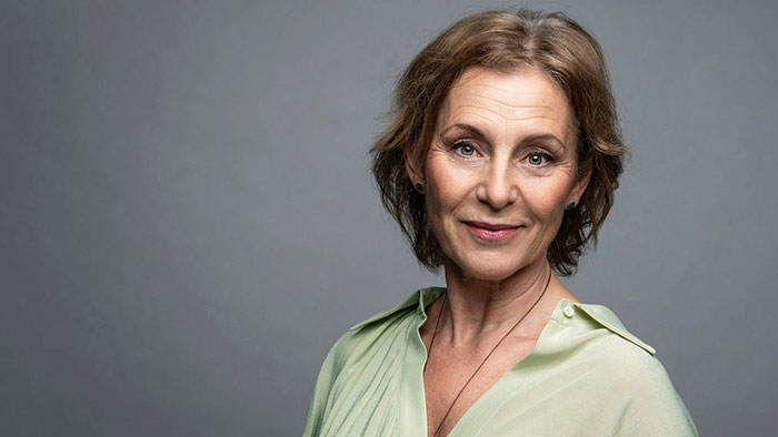 Helen Sjöholm in a light green summer blouse. Half-length photo with a gray background.