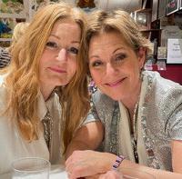 Anna Stadling and Helen Sjöholm are sitting at a table, dressed for show and with their heads together.