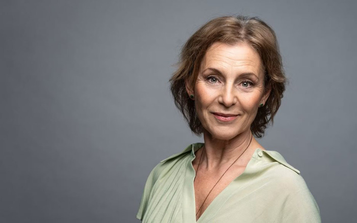 Helen Sjöholm in a light green blouse against a gray background.